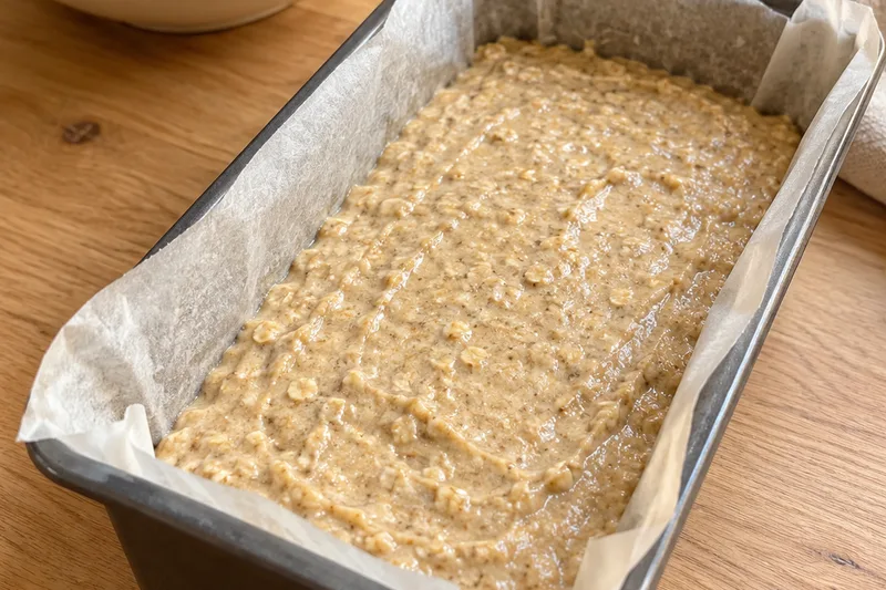 Unbaked oat banana batter smoothed into a parchment-lined loaf pan, filling it about halfway