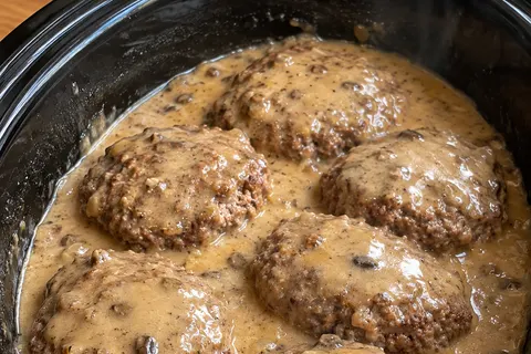 Six tender ground beef patties in creamy mushroom gravy in a black slow cooker