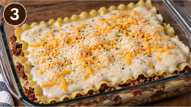 Lasagna layered with noodles, meat, and white cheese sauce in a baking dish