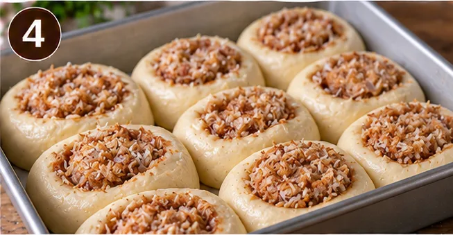 Unbaked coconut-filled dough rolls arranged in a baking pan