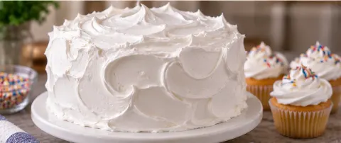 Cake frosted with fluffy, glossy 7-minute frosting alongside frosted cupcakes