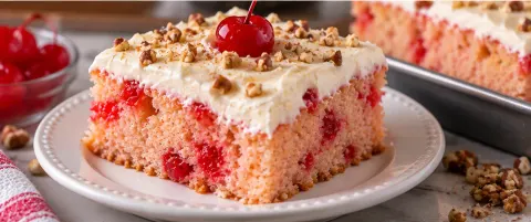 Slice of maraschino cherry cake with whipped frosting, chopped pecans, and a cherry on top