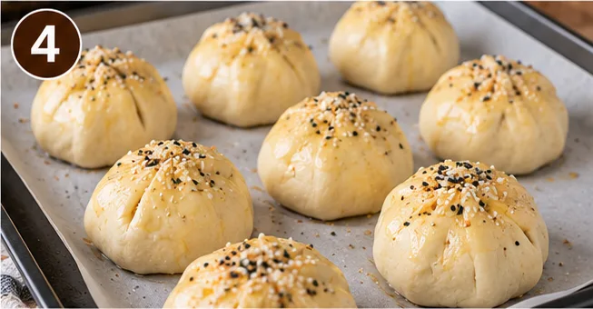 Sealed cheeseburger bomb dough balls brushed with egg wash and topped with sesame seeds, ready to bake