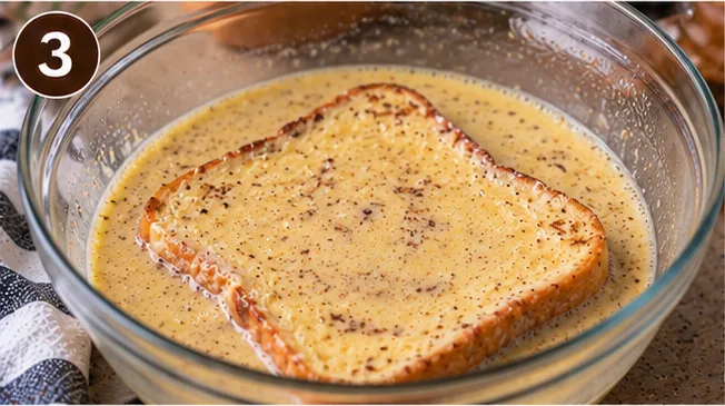 A slice of bread soaking in cinnamon custard in a glass dish