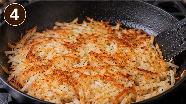 Shredded potatoes cooking into a golden crust in a skillet