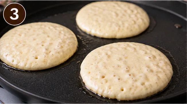 Pancakes cooking on a griddle with bubbles forming on the surface