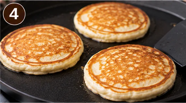 Golden brown pancakes cooking on a griddle after being flipped